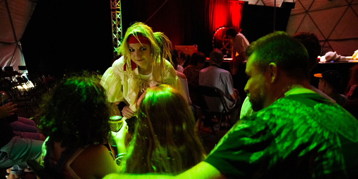 a pirate in natural colors is talking with audience members. there is green and other fun colors surrounding them