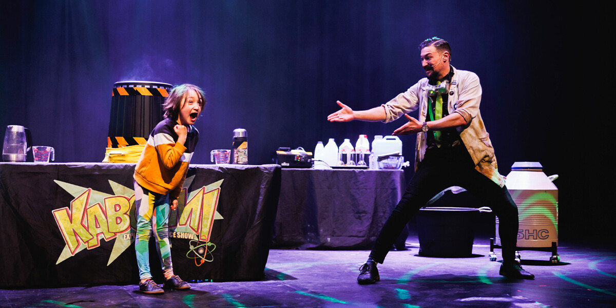 Live show image with performer gesturing to volunteer on stage celebrating.