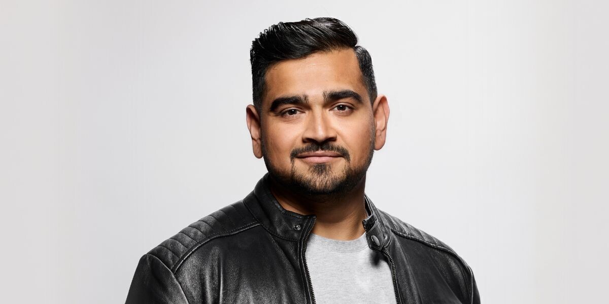Dilruk Jayasinha - Gratitude Guy–Dilruk smiles in front of a white background, he wears a black leather jacket.