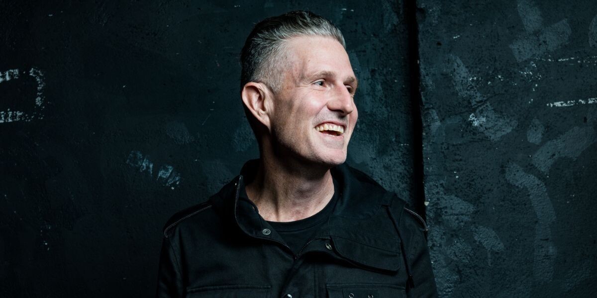 Wil Anderson - Whatchu Talkin' 'Bout Wil?–Wil wears a dark jacket, looks to the right while laughing