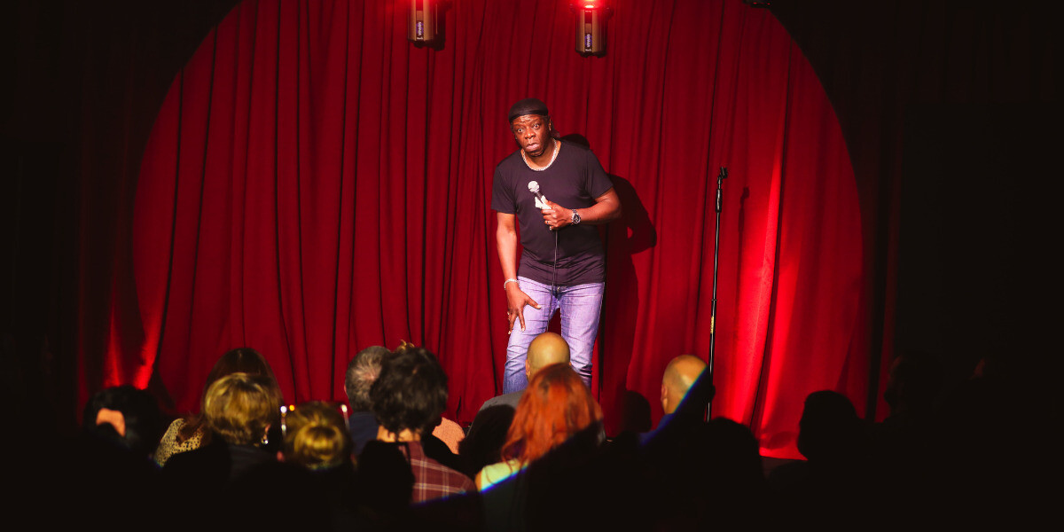 Comedians Ting Lim, Xavier Susai, Ivan Aristeguieta, Dilruk Jayasinha, Andy Saunders, and Joe White pose on stage for a selfie with a cheering, packed theatre audience after a live stand-up show. The performers are smiling and gesturing enthusiastically under bright stage lights, celebrating a sold-out FRINGE WORLD Perth event.