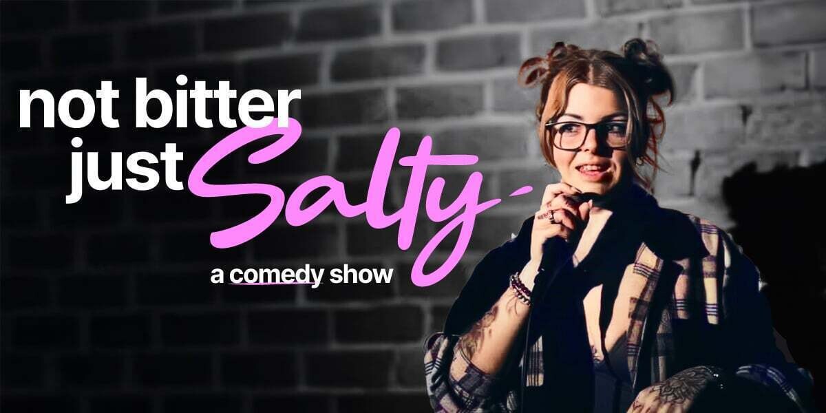 NOT BITTER, JUST SALTY–Promotional poster for Not Bitter, Just Salty – A Comedy Show at FRINGE WORLD Perth. A woman with glasses and tattoos holds a microphone while performing in front of a brick wall. Bold white and pink text reads “not bitter just Salty – a comedy show.” A “Parental Advisory” label at the bottom warns “Leave your kids at home or in the car.”