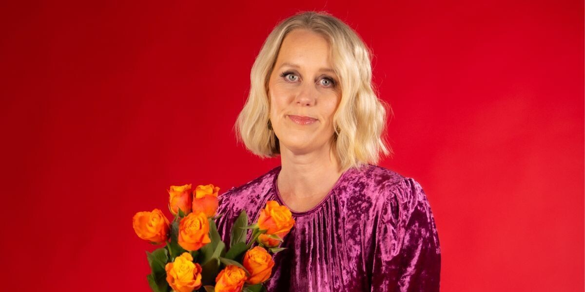 Claire Hooper - fun show xx–Claire is in front of a red background, she holds orange flowers and has a soft smile