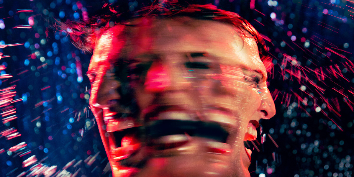 The Kaye Hole - A blurred photo of Reuben Kaye, multiple face effect expresses intensity. Red lighting and splashes of water convey dynamic motion against a dark background.