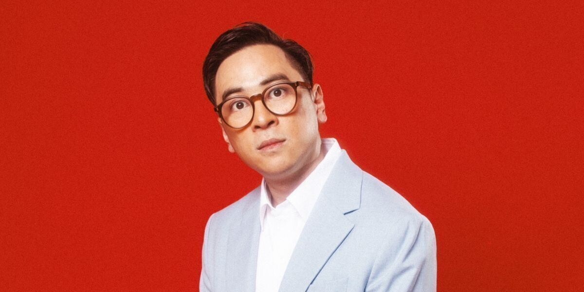 Michael Hing - Real Human Man–Michael wears a grey suit and glasses; he has an inquisitive look and there is a red background