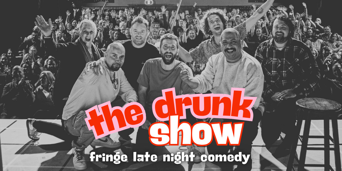 Black-and-white photo of a group of comedians kneeling and sitting at the front of a stage, posing together while a cheering audience fills the background. Bold red and pink text across the bottom reads “the drunk show,” with “fringe late night comedy” written underneath in white.
