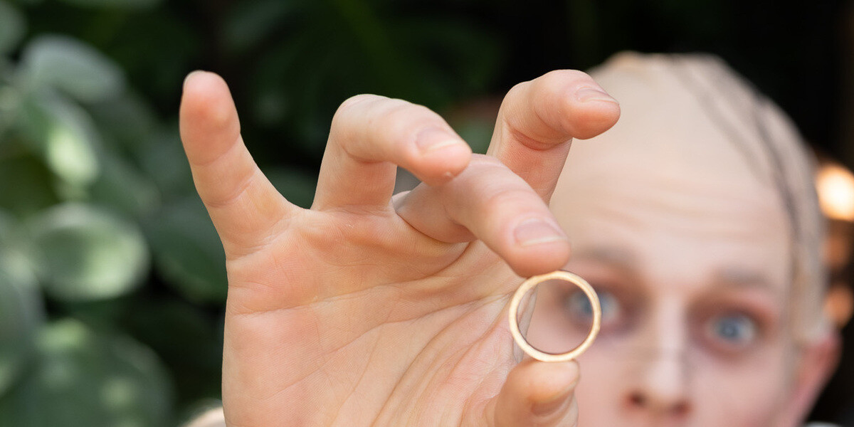 My Precious! The Cabaret–Blurred image of character G'lem, looking into the camera through a golden ring held above his head in foreground.