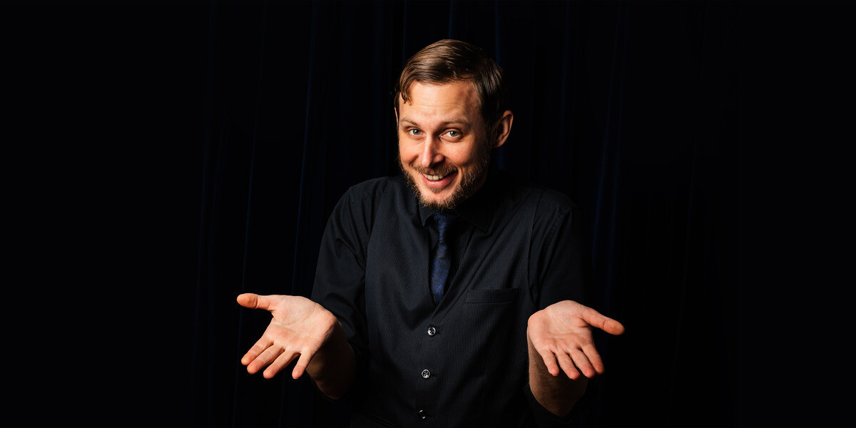 Magical Hands and Magical Feats with Stuart Lightbody–Magician resting his chin on a wooden hand he is holding.