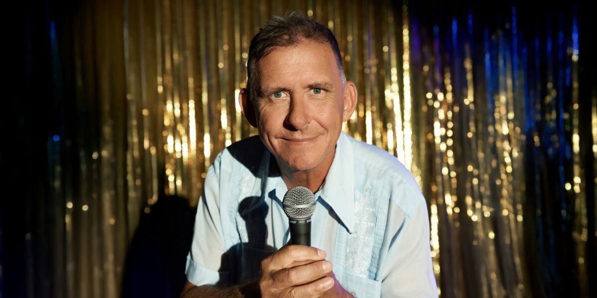 Pete Rowsthorn - Too Keen–Pete holds a microphone; he wears a blue shirt and is in front gold tinsel background.
