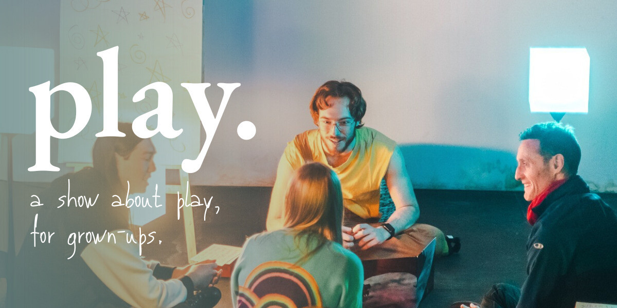 a person with scruffy ginger hair, a yellow shirt and brown dungarees sits on the floor, mid-conversation with three other people who sit surrounding him. over the top of the left side of the image reads the heading 'play.' in large serif font, and the subheading 'a show about play... for grown ups.' in a smaller handwritten font.