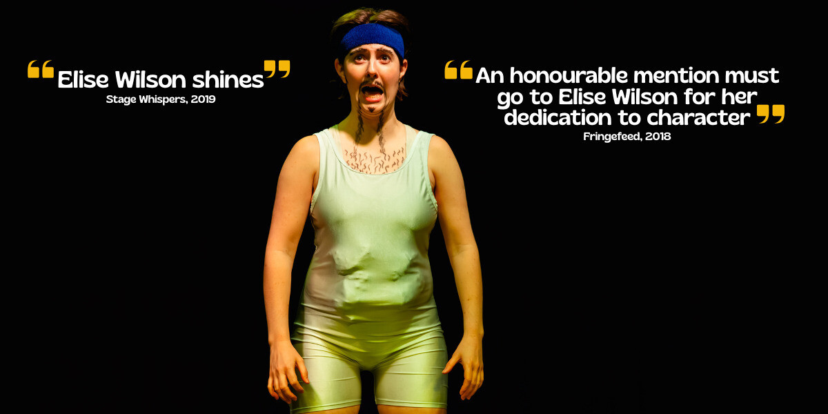 Person stands on stage smiling, wearing a pastel tracksuit and a yellow headband. Purple stage lighting highlights them against a dark background, suggesting a live performance or theatrical setting.