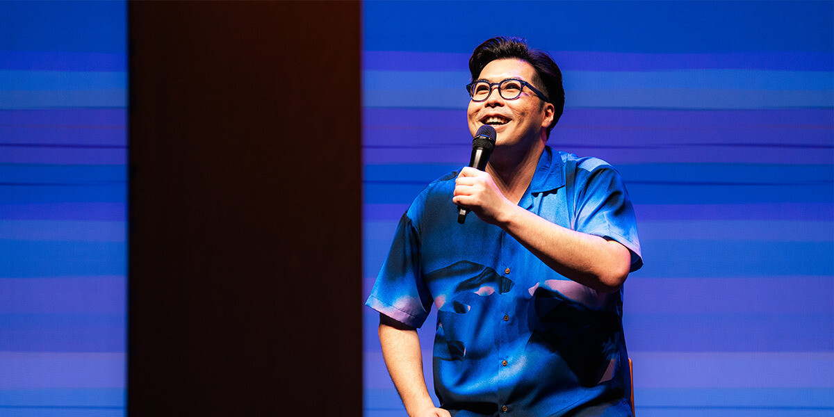 Photo of Jenhan on stage with a mic in hand looking joyous.