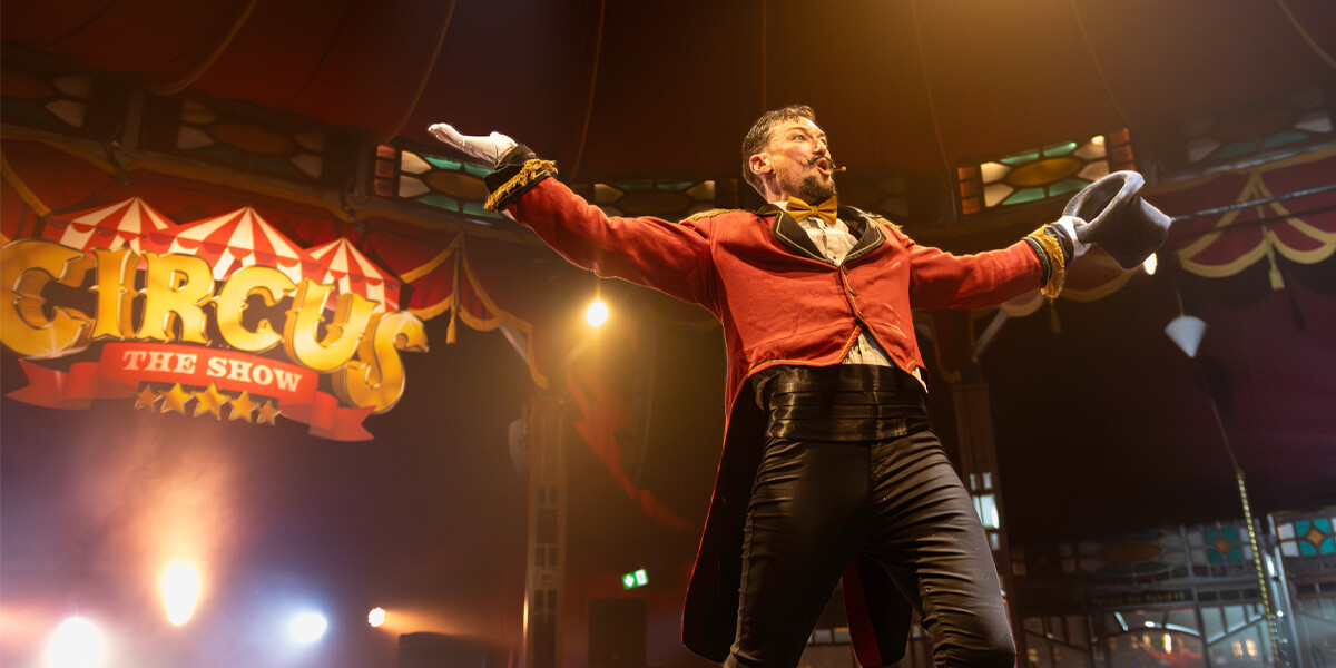Ringmaster character taken off top hat and gesturing towards audience. Live shot from the show.