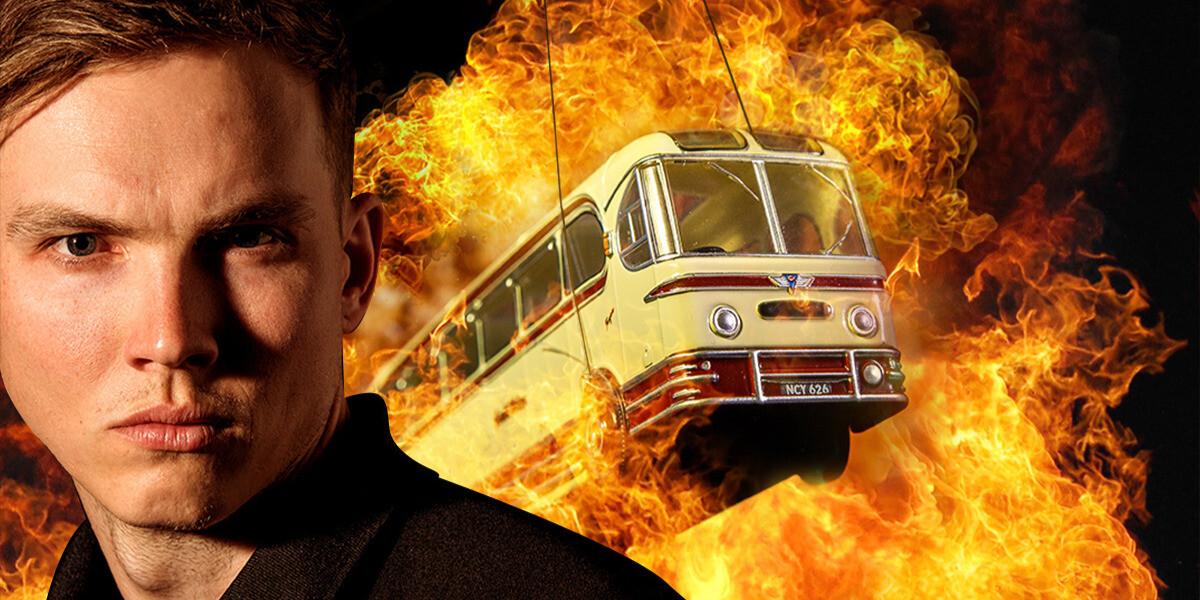 Speed: The Movie, The Play–A man stares out towards the viewer. He is wearing a black shirt. Behind him, a small toy bus on string jumps through an explosion of fire.