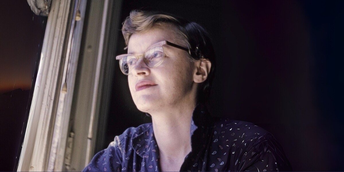 Portrait of Connie Converse in soft light, wearing glasses and looking thoughtfully out a window, half in shadow with a calm, enigmatic expression.