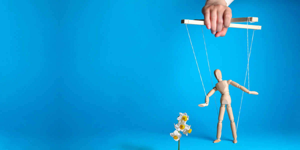 Broken Wheel - A plush brown teddy bear sits upright against a light blue background, wearing a plaid ribbon tied in a bow around its neck. Over the bear’s chest, bold white text reads BROKEN WHEEL. The overall image has a soft, nostalgic feel.