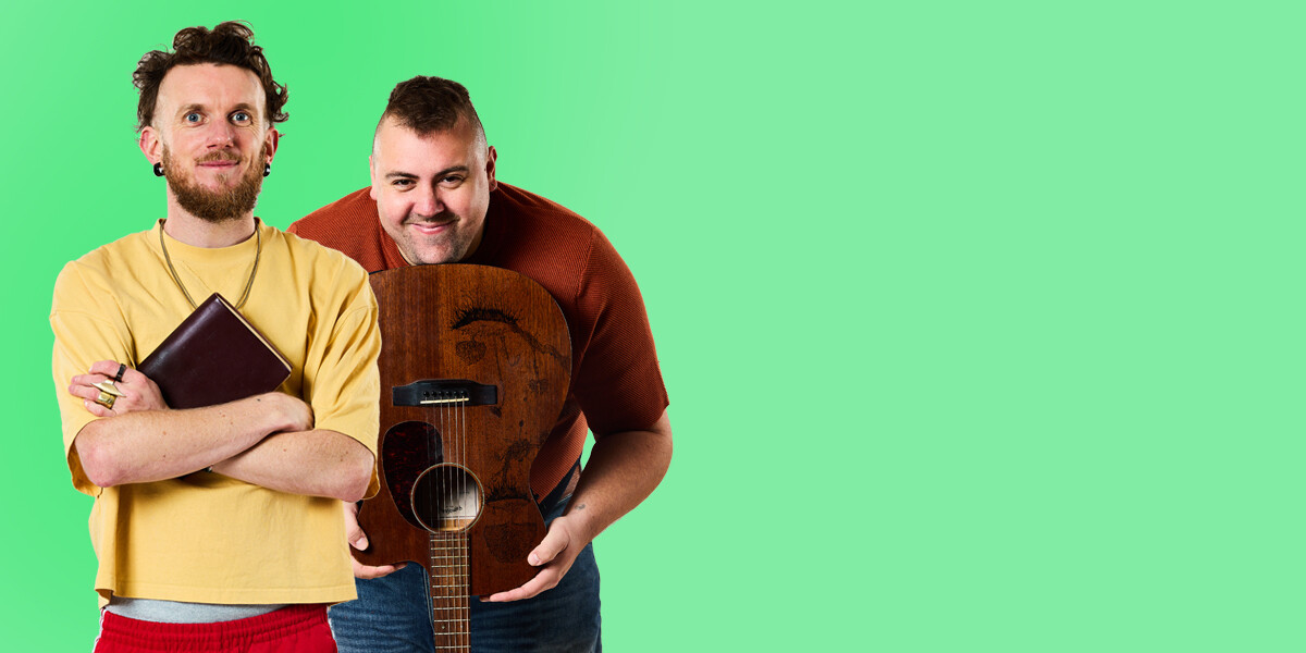 Wright&Grainger's EURYDICE–A man in a yellow shirt, with a beard smiling holding a leather-bound book, and a man smiling, holing a guitar.