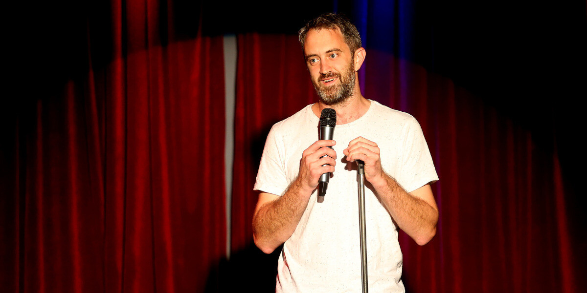 Male comedian Kel Balnaves microphone in hand performing on stage